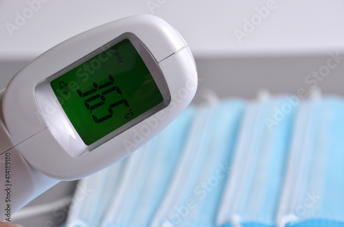 Non-contact thermometer and masks on a gray background.