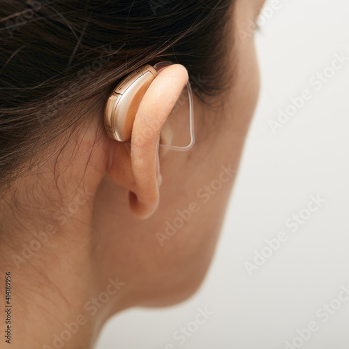 Woman wearing in latest generation hearing aid behind the ear. Hearing solution for adult people with deafness