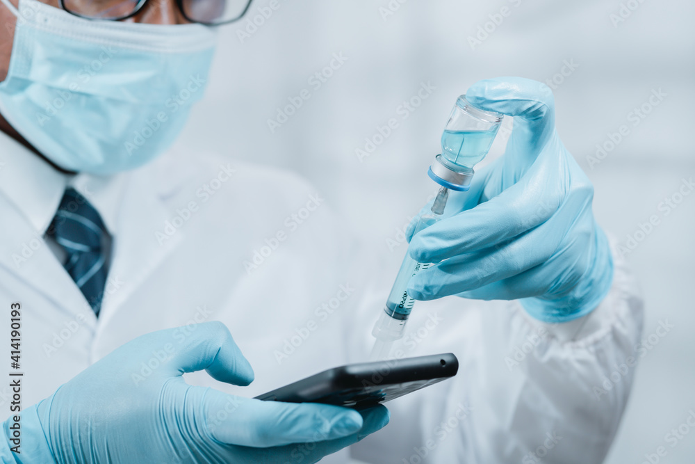 A doctor or scientist in the COVID-19 medical vaccine research and development laboratory holds a syringe with a liquid vaccine to study and analyze antibody samples for the patient. A doctor or scientist in the COVID-19 medical vaccine research and development laboratory holds a syringe with a liquid vaccine to study and analyze antibody samples for the patient.