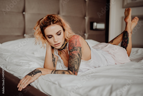 Portrait of a happy beautiful girl with tattoos. The woman is lying in bed. © vitleo