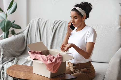 Cuadro en lienzo Angry young woman opening carton box and talking on phone