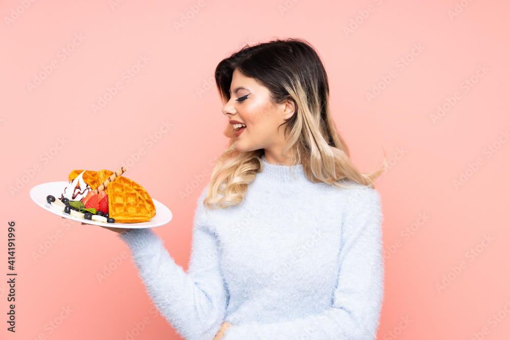 Teenager girl holding waffles on isolated pink background with happy expression