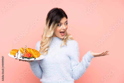 Teenager girl holding waffles on isolated pink background with surprise facial expression
