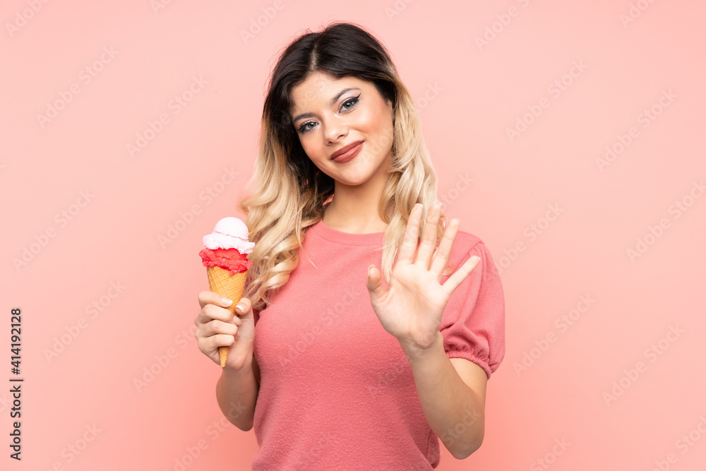Teenager girl holding a cornet ice cream isolated on pink background saluting with hand with happy expression