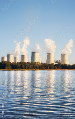 Power plant with smoking chimneys by a lake at sunset.