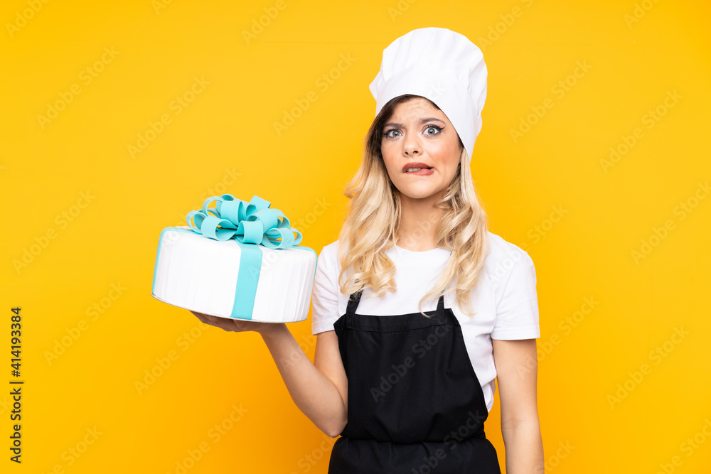 Teenager girl pastry holding a big cake isolated on yellow background having doubts and with confuse face expression Teenager girl pastry holding a big cake isolated on yellow background having doubts and with confuse face expression