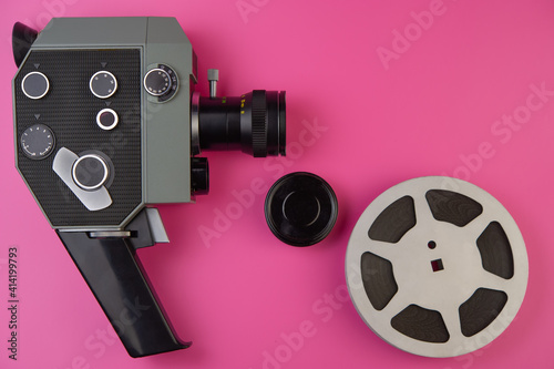 vintage movie camera lies on a pink background and a reel of film.