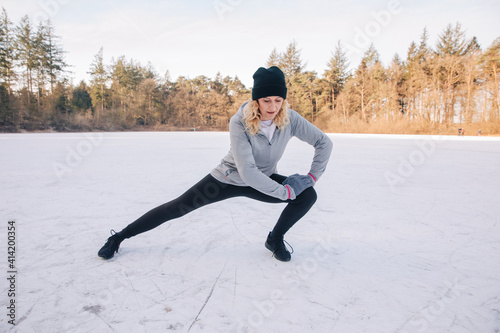 Woman is stretching outside in front of a frozen lake. Sport in winter. Workout in snow. Activities in winter when it's cold 