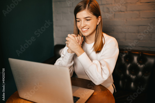 Beautiful blond girl sitting in cafe with laptop, smiling at camera.