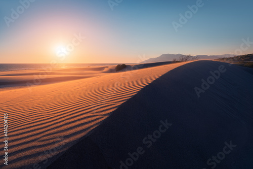 Fototapeta Naklejka Na Ścianę i Meble -  Atmospheric and mystical moody light of the sunset sunbeam illuminated the slope of a sand dune somewhere in the depths of the Sahara Desert