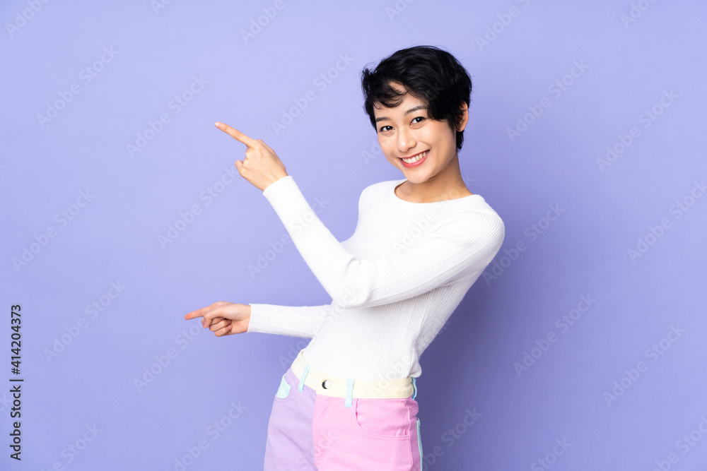 Young Vietnamese woman with short hair over isolated purple background pointing finger to the side and presenting a product Young Vietnamese woman with short hair over isolated purple background pointing finger to the side and presenting a product