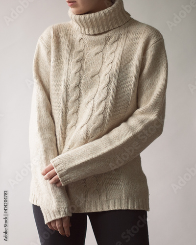Young woman wearing stylish outfit with light sweater and dark trousers on white background.