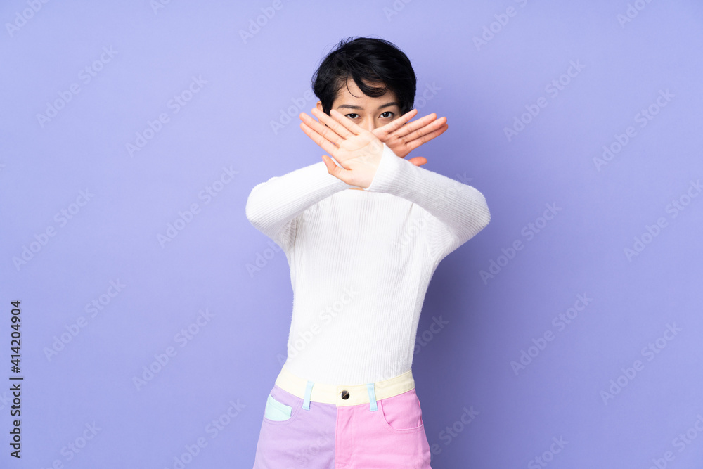 Young Vietnamese woman with short hair over isolated purple background making stop gesture with her hand to stop an act Young Vietnamese woman with short hair over isolated purple background making stop gesture with her hand to stop an act