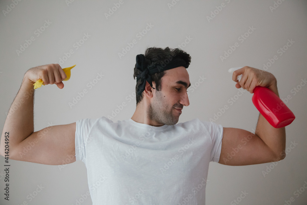 Brunette man holding spray and a duster in his hands doing chores. Man doing cleaning concept. Brunette man holding spray and a duster in his hands doing chores. Man doing cleaning concept.
