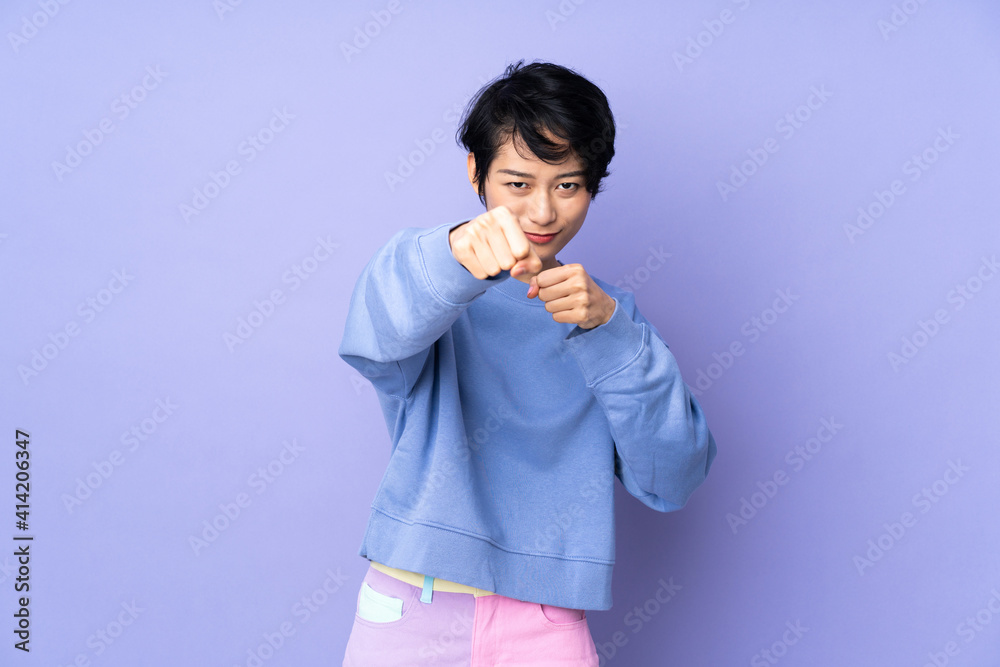 Young Vietnamese woman with short hair over isolated purple background with fighting gesture Young Vietnamese woman with short hair over isolated purple background with fighting gesture
