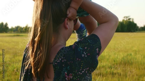 Young mother throws up her chubby funny baby in the air in the summer at sunset.
