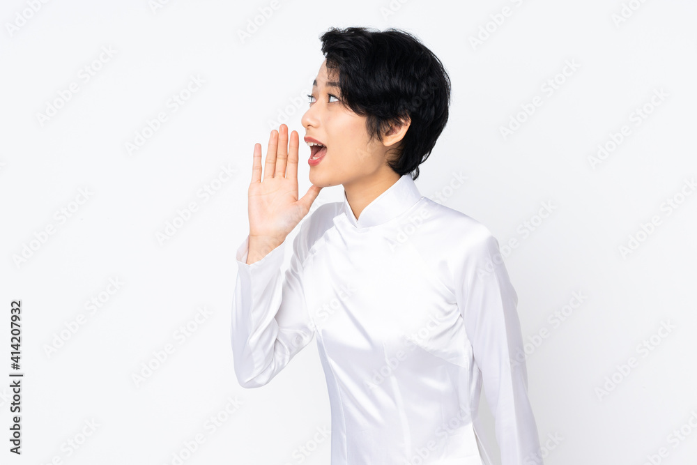Young Vietnamese woman with short hair wearing a traditional dress over isolated white background shouting with mouth wide open to the side Young Vietnamese woman with short hair wearing a traditional dress over isolated white background shouting with mouth wide open to the side