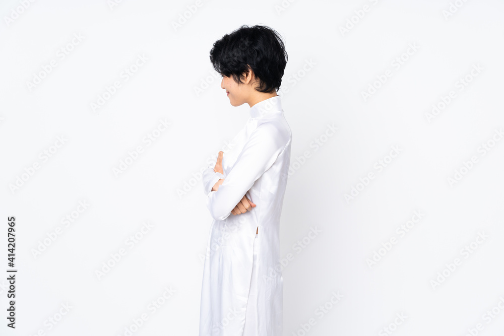 Young Vietnamese woman with short hair wearing a traditional dress over isolated white background in lateral position Young Vietnamese woman with short hair wearing a traditional dress over isolated white background in lateral position