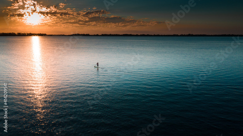 Vista Aérea de una persona sobre un Bote o Kayac, Stand Up Paddle sobre el mar, lago junto a un hermoso atardecer