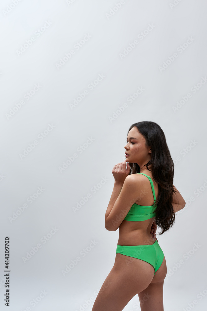 Back view of sensual young woman with slim body wearing green underwear turning her head to side while posing isolated over light background Back view of sensual young woman with slim body wearing green underwear turning her head to side while posing isolated over light background