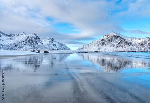 Snowy mountains and blue sky with clouds reflected in water in winter. Arctic sandy beach in Lofoten islands, Norway. Landscape with snow covered rocks, nordic sea coast, sand. Nature background 