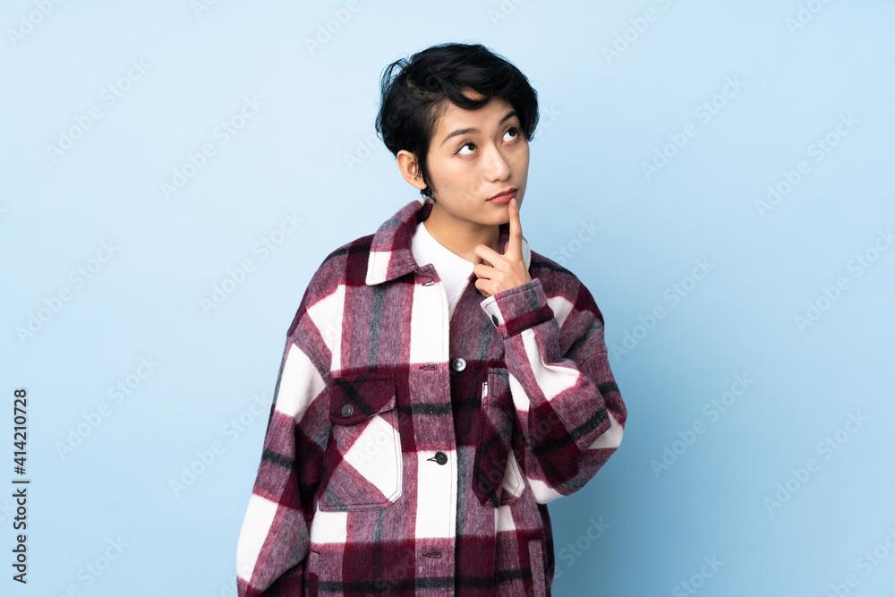 Young Vietnamese woman with short hair over isolated background having doubts while looking up Young Vietnamese woman with short hair over isolated background having doubts while looking up