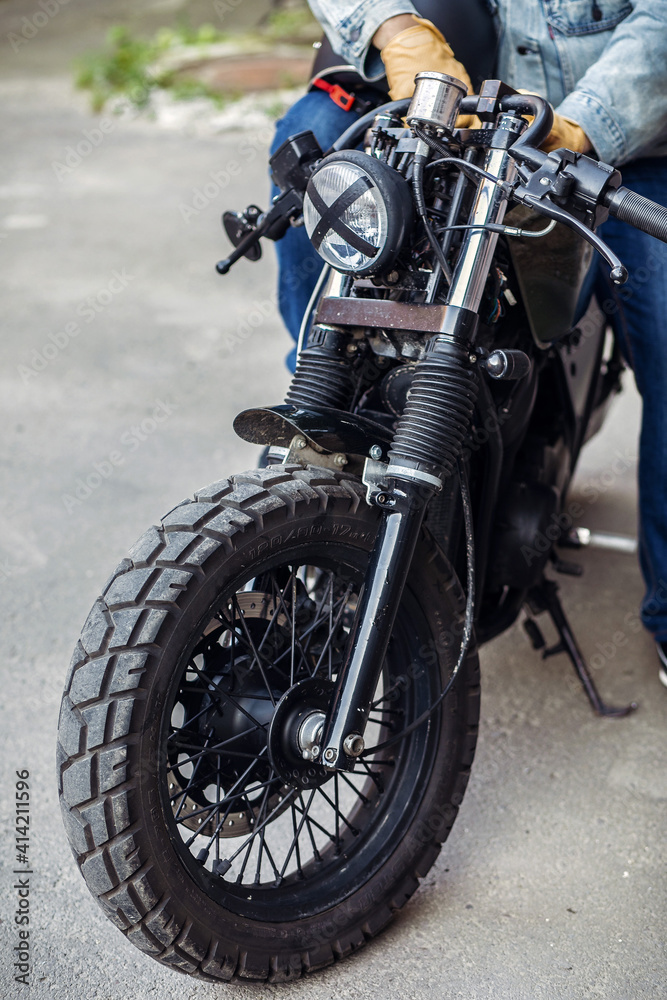 Close up the front part of the motorcycle wheel with the rider sitting with the lamp with tape cross over optic. Motorcycles to order. Casual concept Close up the front part of the motorcycle wheel with the rider sitting with the lamp with tape cross over optic. Motorcycles to order. Casual concept