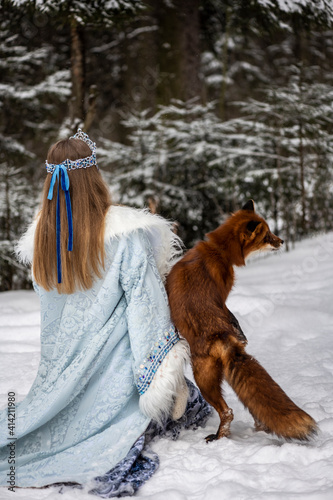 beautiful russian girl in national costume with a red fox in the winter forest