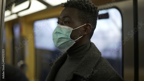 African man standing in subway metro wearing coronavirus mask underground commute