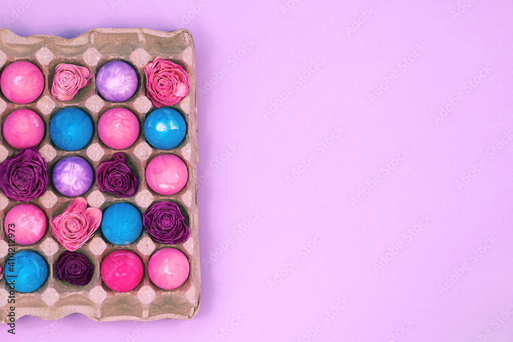 Easter eggs painted with gouache and dried roses in egg box on violet pink background, top view copy space Easter eggs painted with gouache and dried roses in egg box on violet pink background, top view copy space