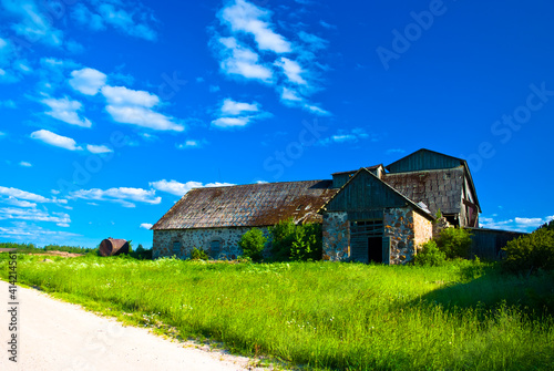 an old stone abandoned building against a blue sky, with a green meadow and a road in the foreground