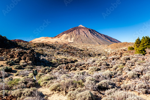 Silhouette of volcano del Teide against blue sky and female hiker with backpack. Pico del Teide mountain in El Teide National park. Tenerife, Canary Islands, Spain