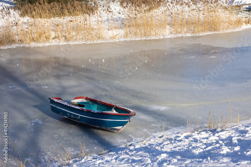 Fotografie, Obraz Frozen ditch with wooden row-boat lying on the ice