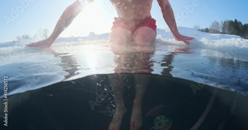 Winter swim, cold treatment. Young man swims in the winter lake with icy water during cold sunny day. Split above under composition with ice floating in the water photo