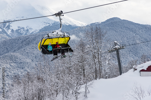 SOCHI RUSSIA - JANUARY 30, 2021: Unknown skiers on chairlift "Skazka" with mountain background in Rosa Khutor ski resort. Cloudy snow weather. Sochi, Russia