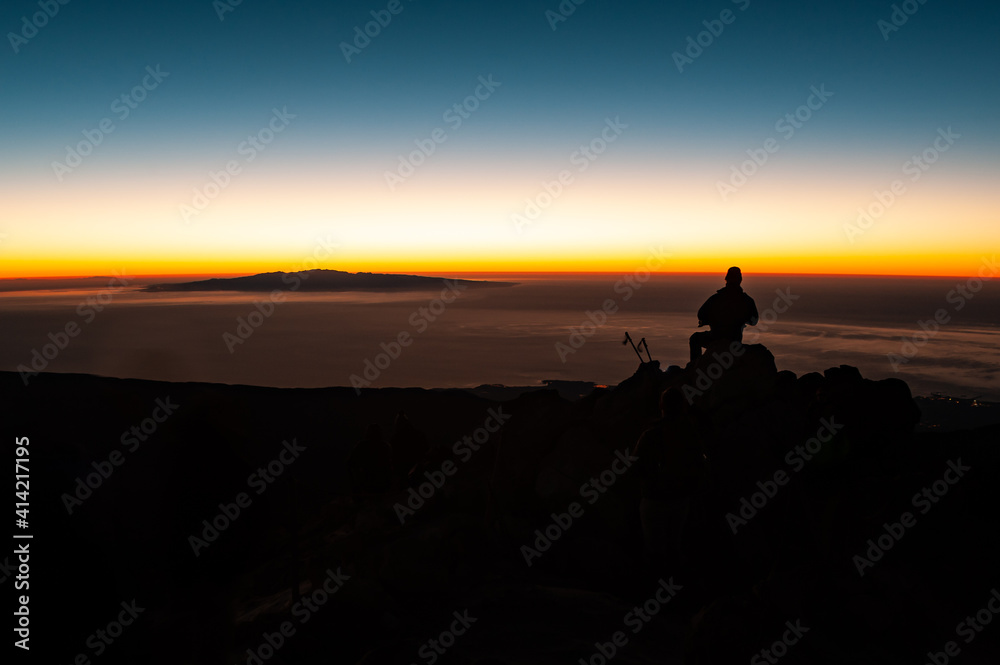 Tourist man with headlamp at dawn sitting and waiting for sunrise at Pico del Teide mountain in El Teide National park. Tenerife, Canary Islands, Spain