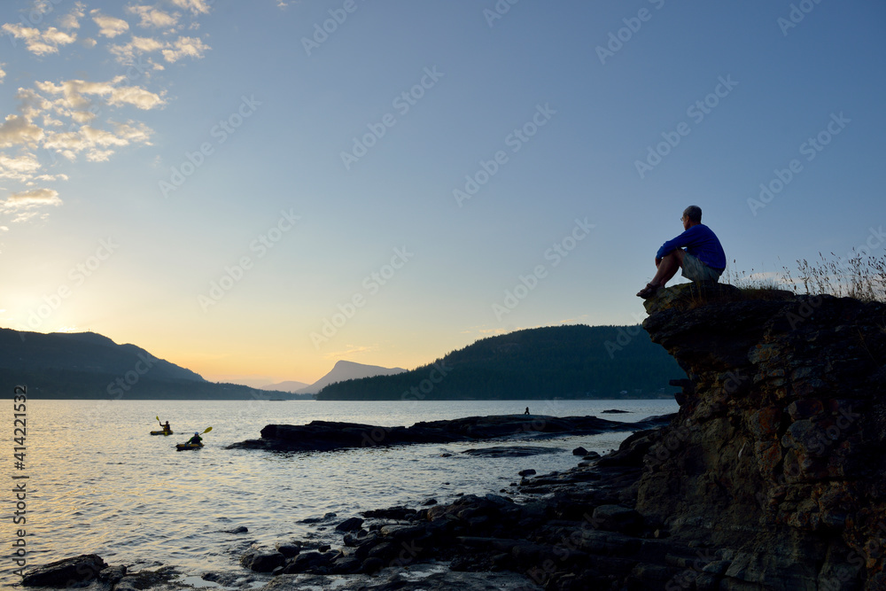 Canada, British Columbia, Russell Island. Man watching kayakers at sunset.