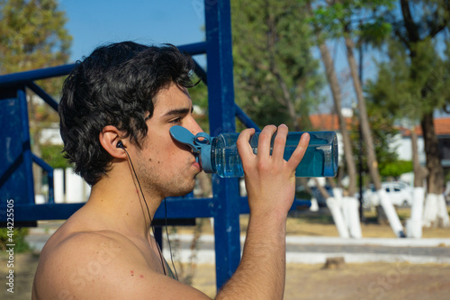 shirtless man drink water in park while exercise