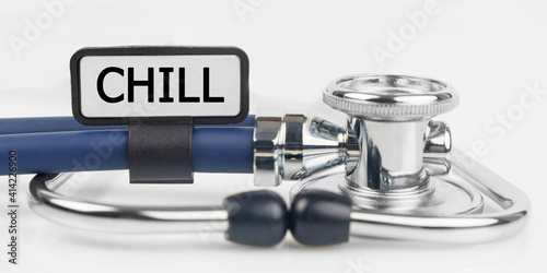 On the white surface lies a stethoscope with a plate with the inscription - CHILL