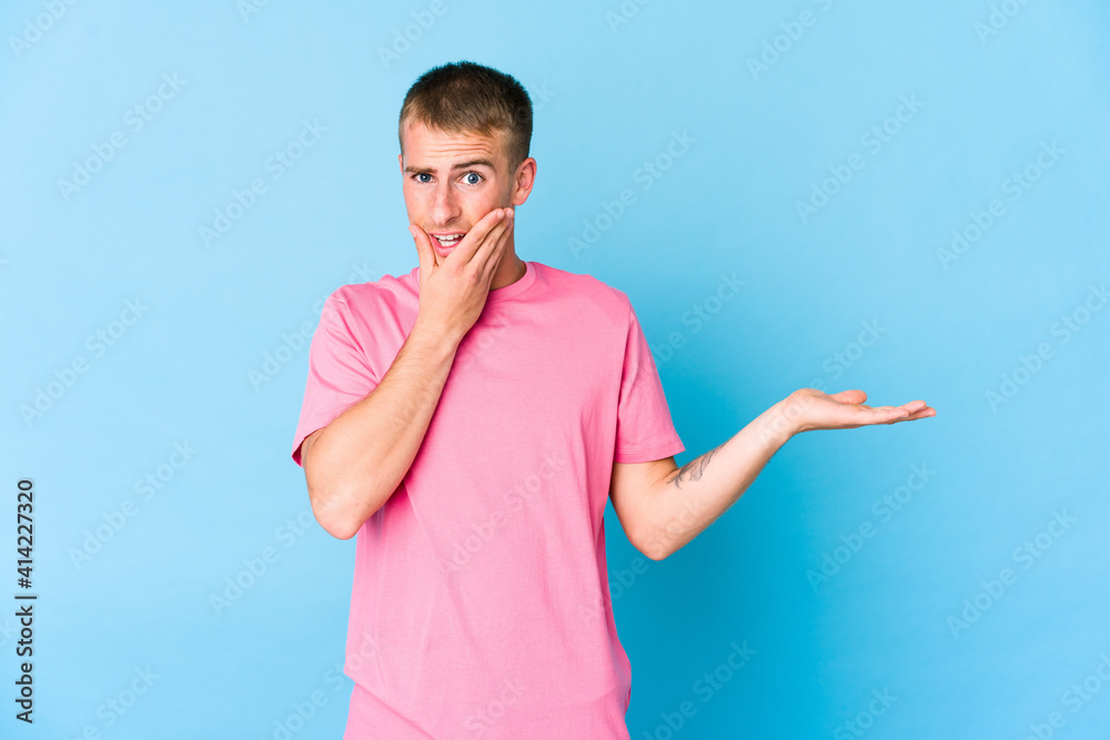 Young caucasian handsome man holds copy space on a palm, keep hand over cheek. Amazed and delighted. Young caucasian handsome man holds copy space on a palm, keep hand over cheek. Amazed and delighted.