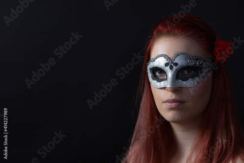 Low key portrait of beautiful redhead young woman posing with silver carnival mask. Horizontally. 