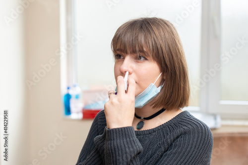 Obraz na plátne Young woman with sickness using nasal spray for protection against coronavirus while she is at work