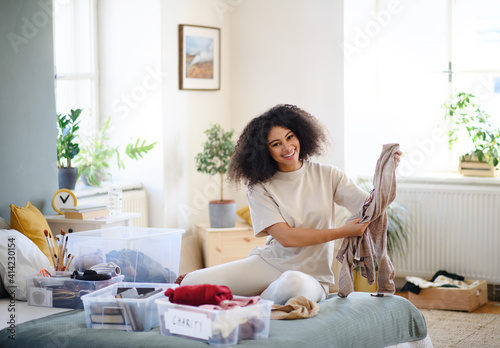 Young woman sorting clothing indoors at home, charity donation concept.