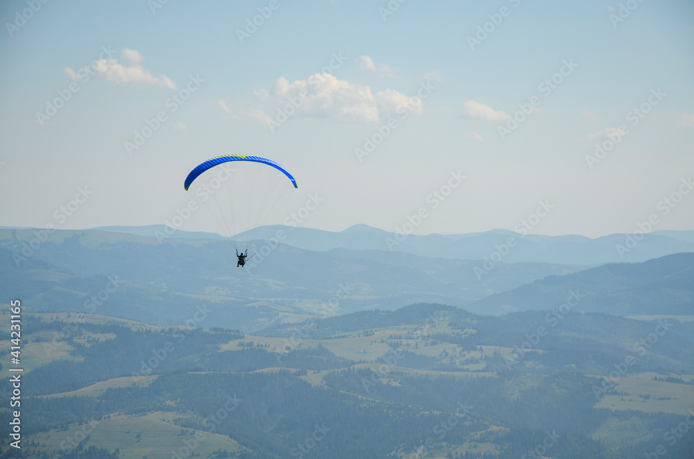 Paraglider flies in the sky over the mountains on a bright sunny day. Paragliding in the sky. Extreme sport. Paraglider flies in the sky over the mountains on a bright sunny day. Paragliding in the sky. Extreme sport.