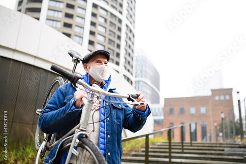 Senior man carrying bicycle outdoors on street in city, coronavirus concept.