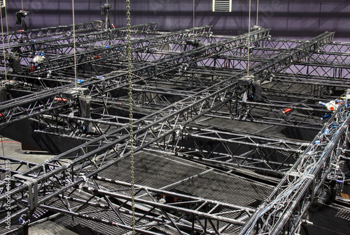 Black steel trusses are lifted by chain hoists. Installation of professional rigging equipment for a concert show.
