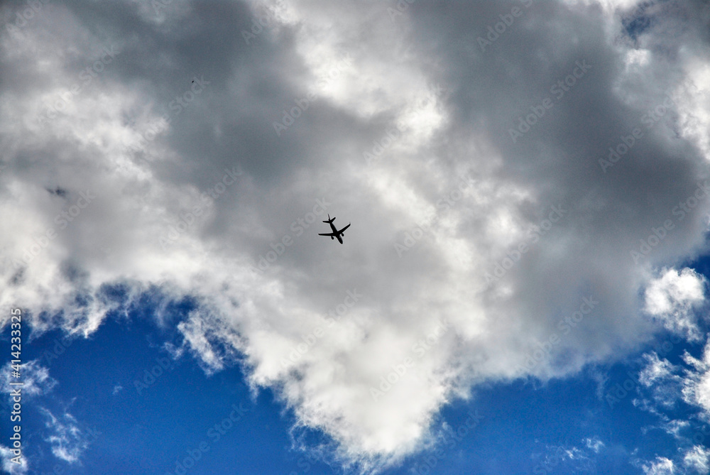 Airplane flying between clouds, blue sky and white clouds.