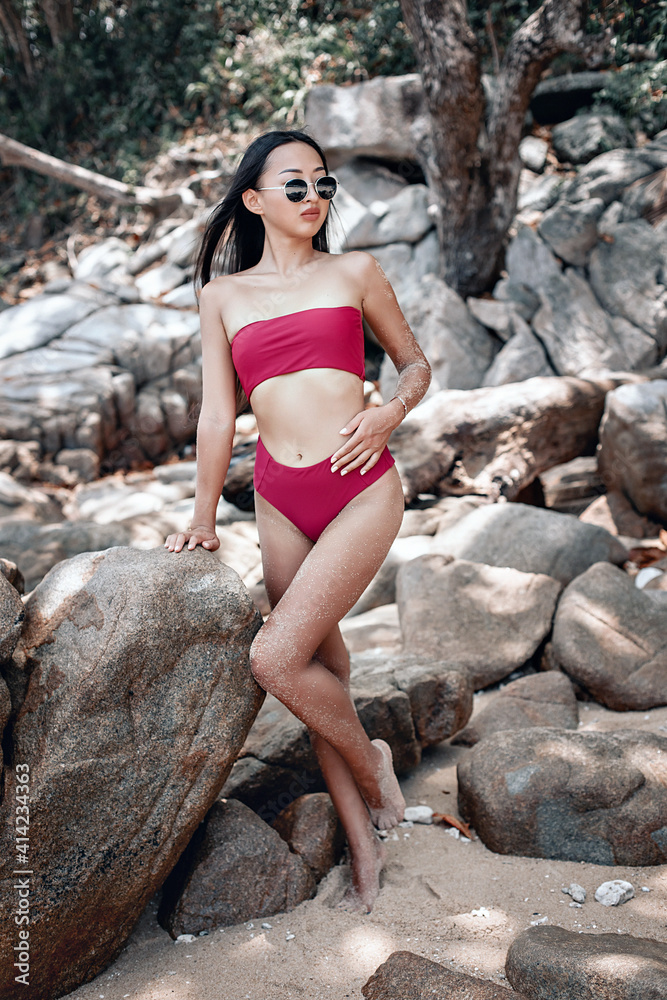 Adorable beautiful fit woman in a burgundy bikini is posing next to huge cobblestones, portrait, fell height Adorable beautiful fit woman in a burgundy bikini is posing next to huge cobblestones, portrait, fell height