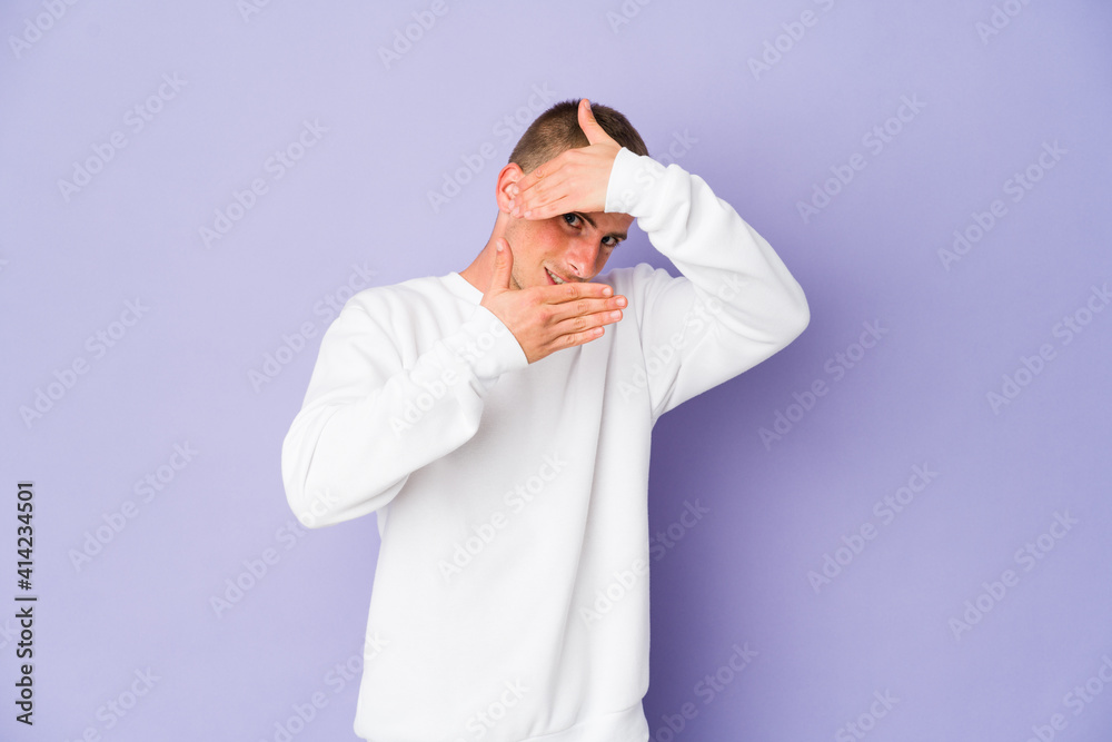 Young caucasian handsome man blink at the camera through fingers, embarrassed covering face. Young caucasian handsome man blink at the camera through fingers, embarrassed covering face.