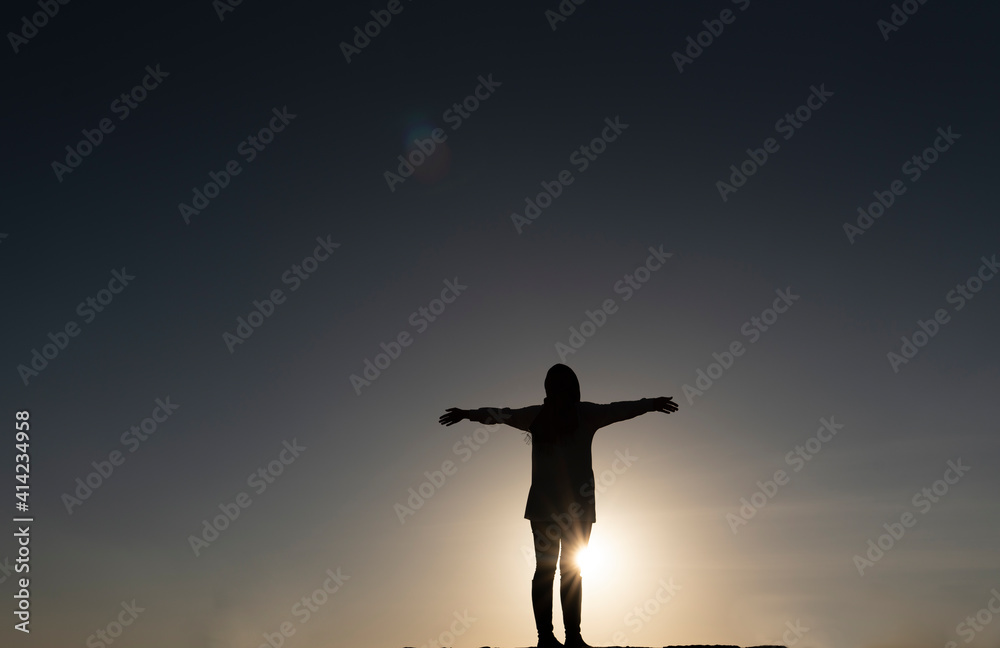 Silhouette of a young dancing woman with long wavy hair in the mountains in the backdrop of the setting sun 